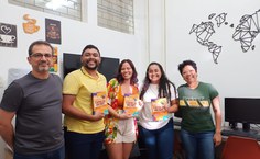 Professor supervisor Denis Rocha entregando os livros físico para os pibidianos junto com a professora Cirlene [de verde] (Arquivo Pessoal)