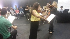 Lílian Pereira (à esq.) regendo a Camerata com o violino e acompanhando sua aluna Claudineide Pereira